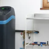Nowoczesny zmiękczacz wody, który może znaleźć się w czołówce rankingu. Urządzenie z niebieskim pasem i panelem sterowania, podłączone do instalacji wodnej.