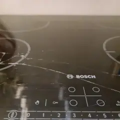 Pęknięta płyta indukcyjna Bosch z widocznymi rysami i pęknięciami na szkle.
