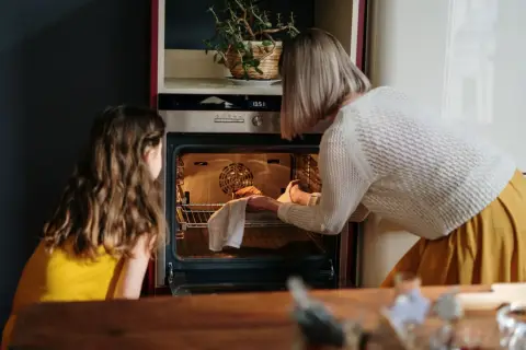 Mama i córka wkładają ciasto do rozgrzanego piekarnika. To ich pierwsze uruchomienie piekarnika po przeprowadzce.
