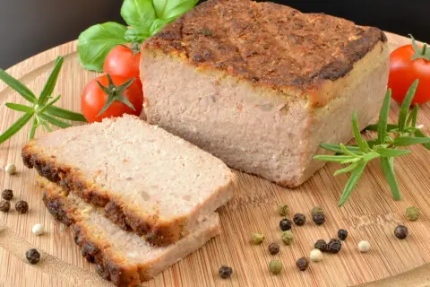 Pyszny pasztet w piekarniku, pokrojony na plastry, z pomidorkami, rozmarynem i pieprzem na desce.
