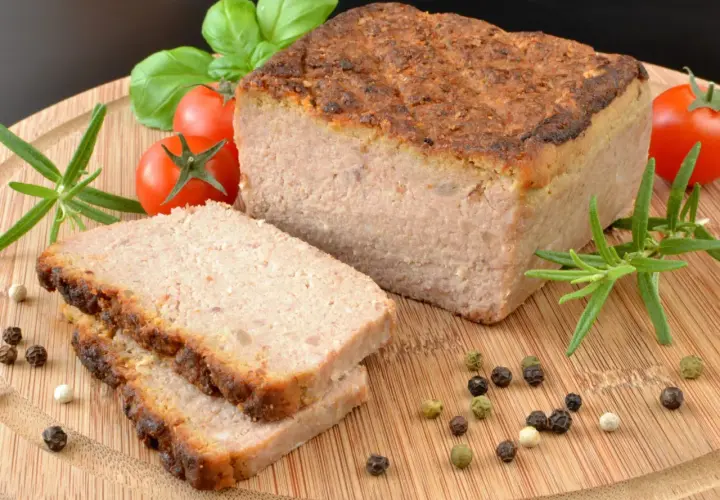 Pyszny pasztet w piekarniku, pokrojony na plastry, z pomidorkami, rozmarynem i pieprzem na desce.