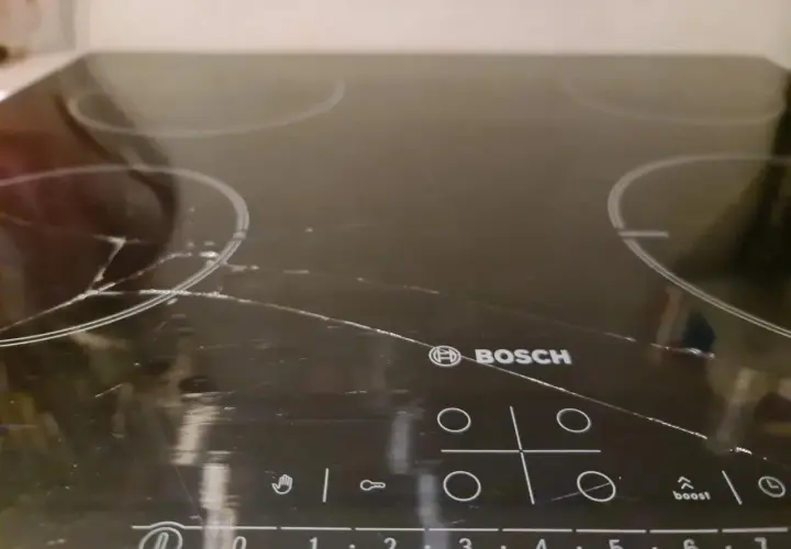 Pęknięta płyta indukcyjna Bosch z widocznymi rysami i pęknięciami na szkle.