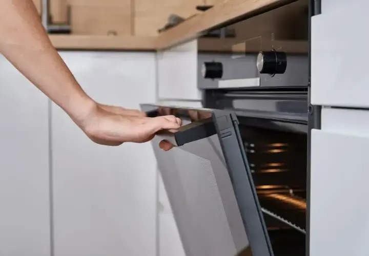 Ręce otwierają piekarnik Amica. Widać pokrętło temperatury i oznaczenia funkcji.
