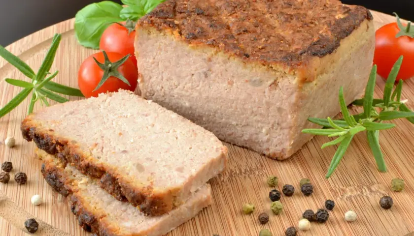 Pyszny pasztet w piekarniku, pokrojony na plastry, z pomidorkami, rozmarynem i pieprzem na desce.