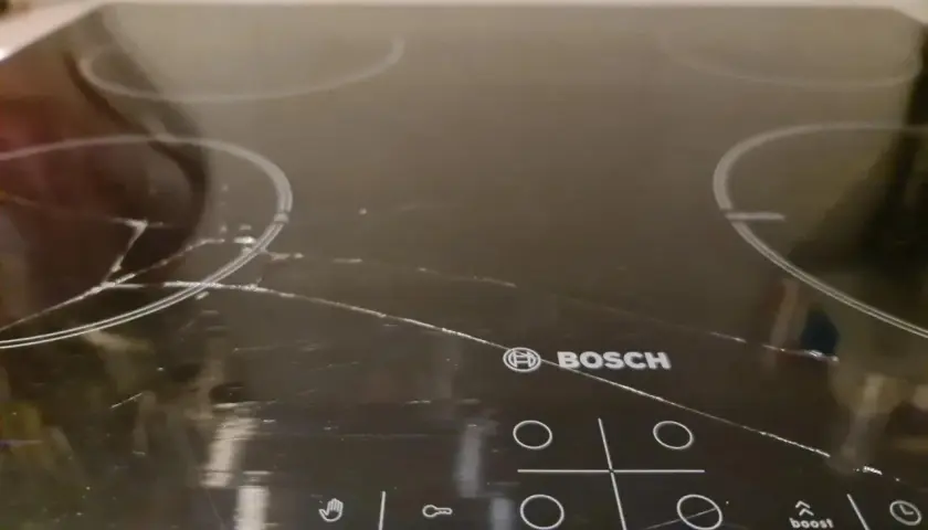 Pęknięta płyta indukcyjna Bosch z widocznymi rysami i pęknięciami na szkle.